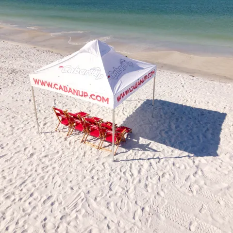 Beach cabana with red chairs on white sand near the ocean.
