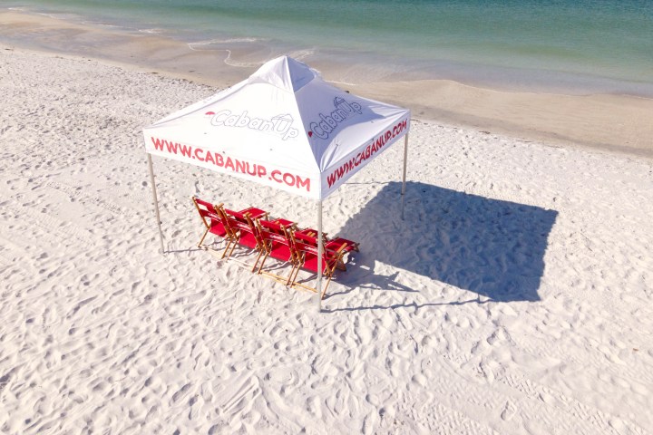 Beach cabana with red chairs on white sand near the ocean.