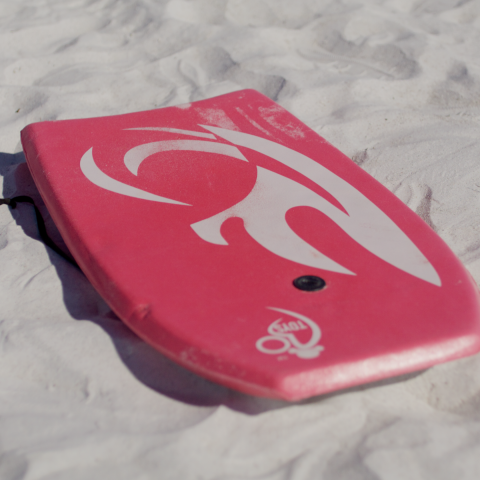Pink bodyboard with abstract design on sandy beach.