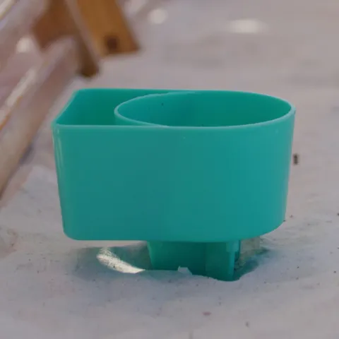 Turquoise plastic object partially buried in sand with blurred wooden structures.