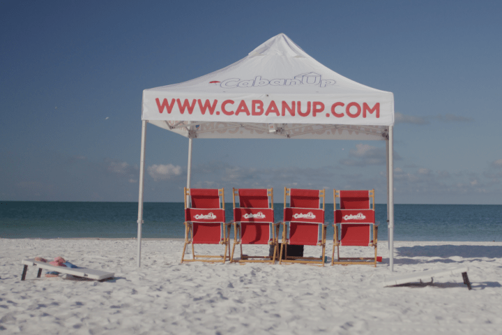 Beach tent with red chairs and website text on sandy shore, ocean in background.