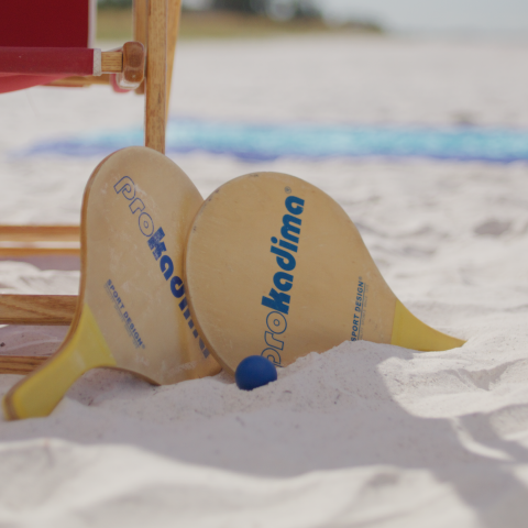 Beach paddle game set on sandy beach near a wooden chair.