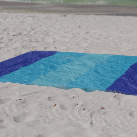 Blue beach blanket on sandy shore with ocean in background.