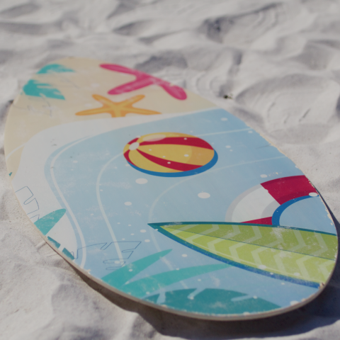 Colorful skimboard with beach designs on white sand.