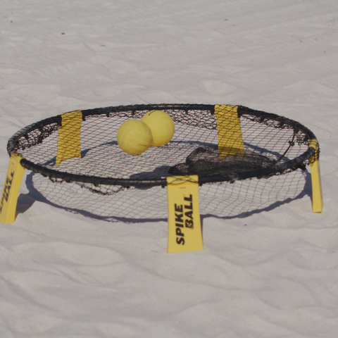 Spikeball net with yellow ball set up on sandy beach.