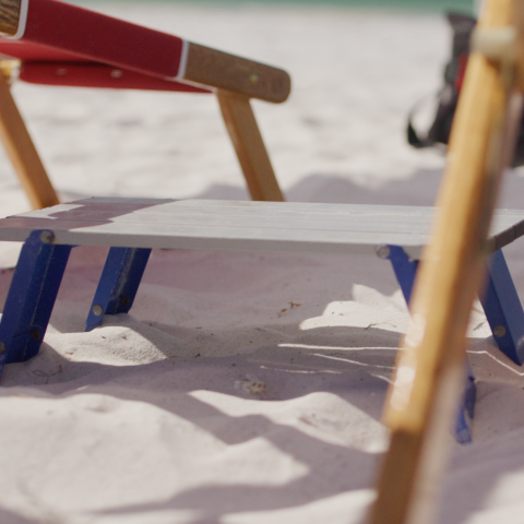 Beach chairs on sand with a small folding table in the middle.