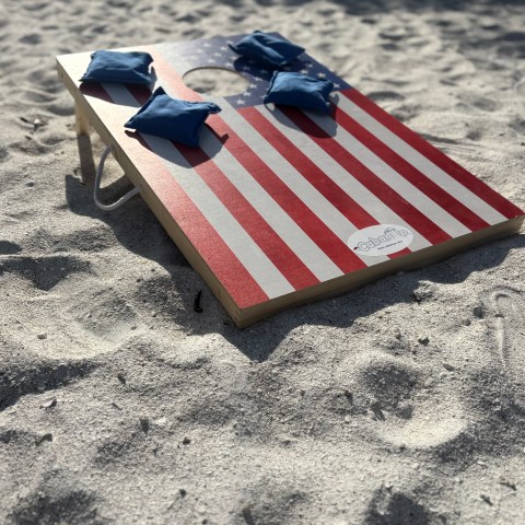 American flag cornhole board with bean bags on sandy beach.
